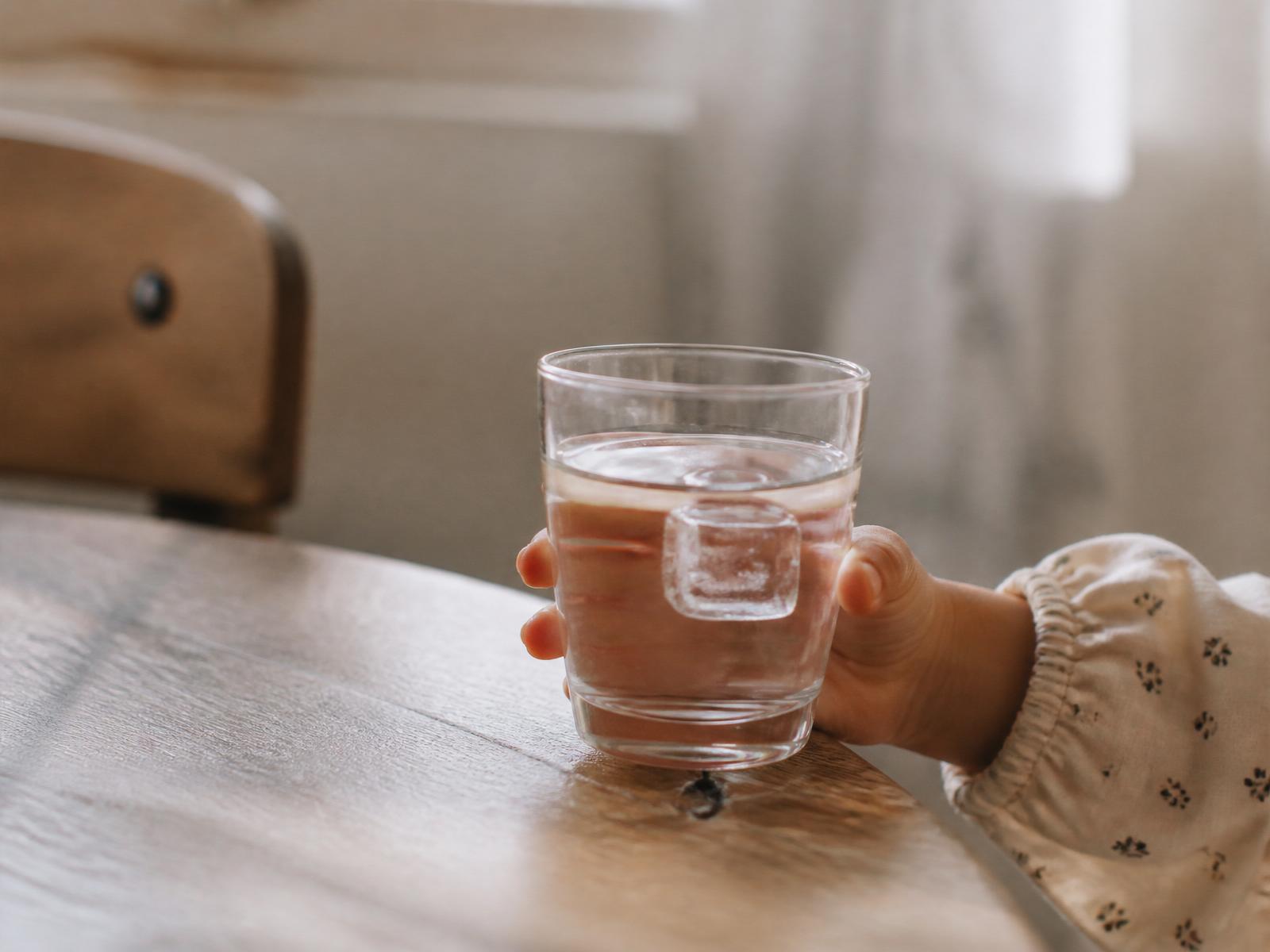 A child's hand holding a glass of water with a single perfect ice cube